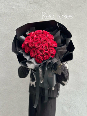A bouquet of red roses wrapped in black paper with a decorative ribbon.