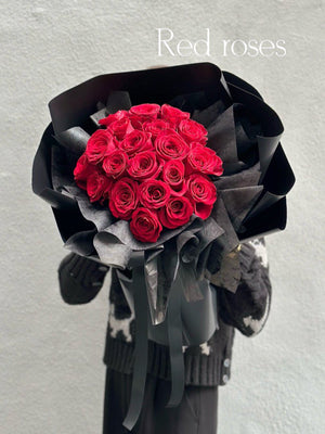 A bouquet of red roses wrapped in black paper with a decorative ribbon.