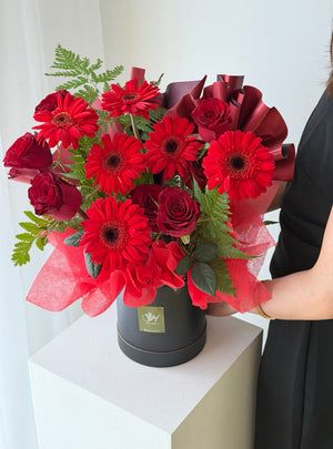 Red Roses and red gerbera and some paku leaf in a black round box, this flower box is perfect for house warming gift, grand opening flower stand gift at Kuala Lumpur and Selangor.