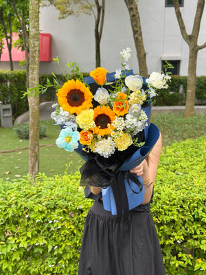 Blue and yellow themed graduation flower bouquet featuring sunflowers and roses holding by a girl at outdoor.