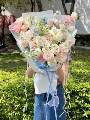 Large blue and pink flower bouquet featuring premium pink roses, blue delphinium, white narcissus, carnations, and seasonal mixed fillers, held by a girl with same-day flower delivery in Kuala Lumpur and Selangor.