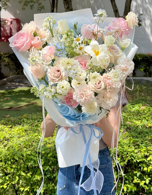 Large blue and pink flower bouquet featuring premium pink roses, blue delphinium, white narcissus, carnations, and seasonal mixed fillers, held by a girl with same-day flower delivery in Kuala Lumpur and Selangor.