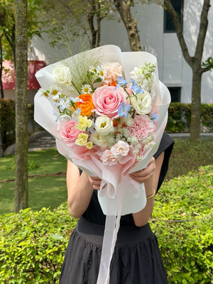 Small pink flower bouquet featuring premium pink roses, blue delphinium, hana white, carnations, and seasonal fillers, held by a girl in a black dress with same-day flower delivery in Kuala Lumpur and Selangor.