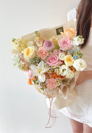 Close-up of a luxurious mixed flower bouquet with soft-colored blooms and intricate wrapping, displayed in a minimalist white setting