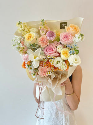 Elegant floral arrangement featuring roses, tulip, scabiosa, carnations, chamomile and mixed of other flowers wrapped in cream paper with pink ribbon.