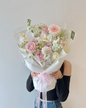 Close-up of a beautifully arranged pastel flower bouquet with soft pink and white blooms, wrapped in translucent white paper and tied with a sheer pink ribbon.