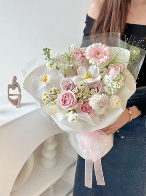 Delicate spring bouquet with pink and white flowers, including roses and daisies, held by a woman dressed casually against a light background.