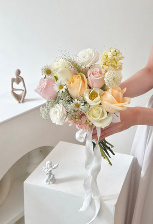 Soft pastel bridal bouquet for ROM season featuring champagne rose, white rose, pink rose, white tulip, yellow matthiola, hand-tied with an elegant white ribbon—perfect for intimate wedding ceremonies.