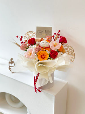 Floral display for a grand opening, showcasing a smiling orange Maneki-neko (lucky cat) surrounded by colorful artificial flowers in red, pink, and orange hues.