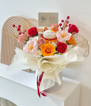 A vibrant flower arrangement featuring an orange lucky cat figurine, designed for a business grand opening. The bouquet includes roses and decorative accents in a white box.