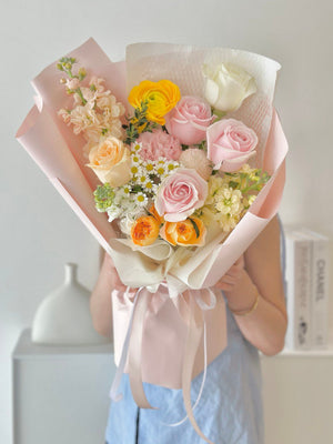 A person holding a bouquet of flowers which includes pink roses, a champagne rose, a white rose, and various other flowers in pink and white shades.