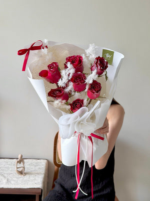 Bouquet of red roses with white accents design for Christmas gift held by a person against a neutral background.