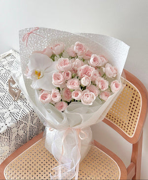 Bouquet of kiss of fairy rose spray flowers wrapped in white wrapper on a chair with a white background.