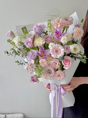Bouquet of pastel purple theme flowers held by a person against a neutral background.