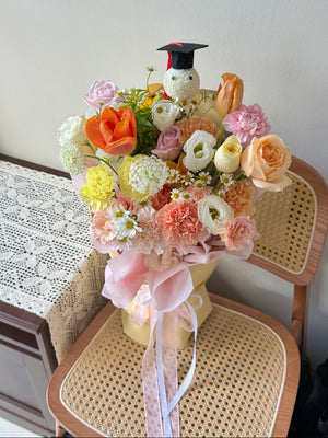 Bouquet of flowers with orange tulip, champagne rose, yellow carnation, pink rose with a graduation ping pong cap perfect for graduation flower bouquet.