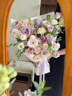 A girl is holding her anniversary purple theme bouquet in front of a mirror.