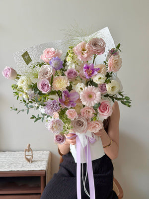 A girl wearing a black dress is holding a bouquet of pastel purple theme flowers for her birthday celebration at Kuala Lumpur.