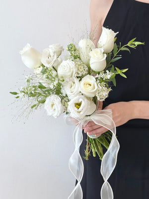 A person in a black dress holding an elegant white bouquet of roses and eustoma, tied with a sheer ribbon at her ROM.