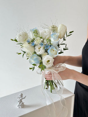 A graceful arrangement of pastel flowers and greenery, designed for ROM brides, tied with a sheer ribbon and held by hand.