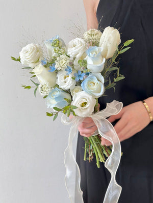 A delicate white roses and oxypetalum blue bouquet with roses and white tulip, perfect for ROM ceremonies, held by a person in a black dress.