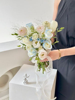 Delicate hand bouquet featuring white roses, eustoma, and soft blue accents, perfect for ROM ceremonies, styled with a modern romantic touch.