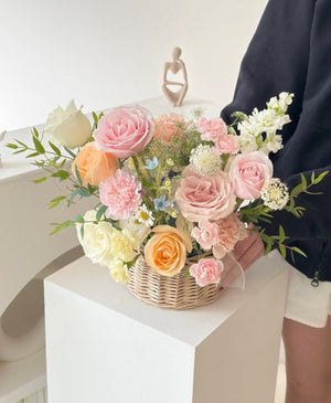 A pastel flower basket with pink, peach, and white roses, carnations, and delicate wildflowers arranged in a woven basket—perfect for a get well soon message or a thoughtful gift.