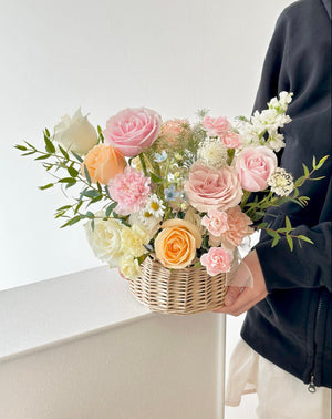 Beautiful hand-arranged basket of fresh pastel blooms, including roses and carnations, placed on a white pedestal—an uplifting and graceful gift for recovery or celebration.