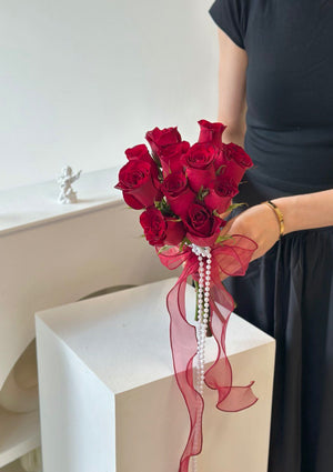 Elegant hand-tied red rose bouquet for a wedding ceremony, featuring a bold red ribbon and pearl embellishment.