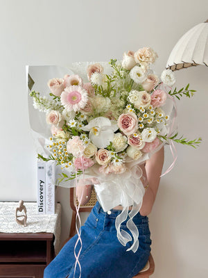 Bouquet of quicksand rose mixed with fillers flowers held by a person wearing blue jeans in a room setting.
