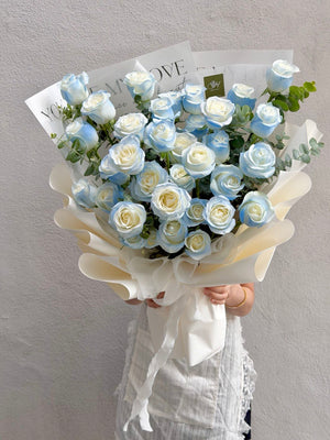 A girl is holding a bouquet of 30 white rose sprayed with light blue perfect for proposal, birthday or anniversaries flower prepared by Hug and Heart Florist Subang Jaya.