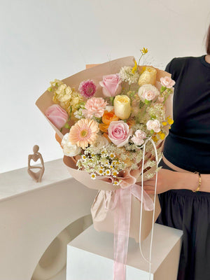 A charming spring-inspired bouquet with mixed fresh blooms, wrapped in nude-toned paper and sheer ribbons.