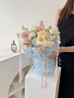 Elegant flower bouquet in shades of blush, ivory, and pale blue, wrapped with transparent film and tied with pastel ribbons, perfect for birthdays, anniversaries, or romantic gestures.
