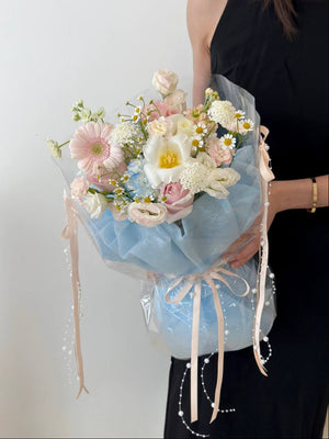 Soft and dreamy mixed flower bouquet with a touch of spring, including dainty daisies, roses, gerbera, and tulip, displayed against a clean white background in a modern setting.