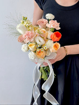A woman in a black dress holds a bridal bouquet of orange tulips and various shades of roses, showcasing elegance and beauty.