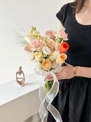 A woman dressed in black holds a stunning bridal bouquet featuring orange tulips and champagne, buttercup, and cappuccino roses.