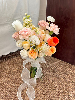 A girl in a black dress presents a beautiful bridal bouquet with orange tulips and a mix of champagne and buttercup roses.