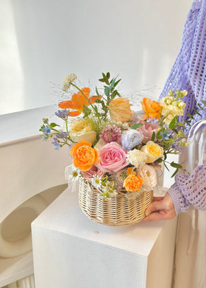 A cheerful basket of flowers placed on a white column, suitable for housewarming or get well soon occasions.