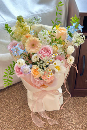 Bouquet of pastel flowers with pink and white ribbons on a carpeted floor.