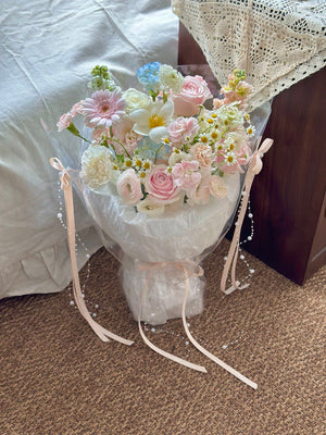 Bouquet of flowers wrapped in white paper with ribbons on a carpeted floor.