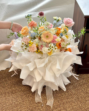 Bouquet of fresh blooms including roses, daisies, and fillers, artistically arranged for a special milestone or celebration held by a person on a carpeted floor.