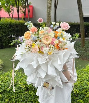 Bouquet of flowers with delicate wrapping, symbolizing love and celebration for a birthday held by a person outdoors.