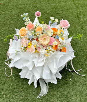 Bouquet of flowers mixed flower arrangement in shades of peach, pink, and white with white ribbons on a green grass background.