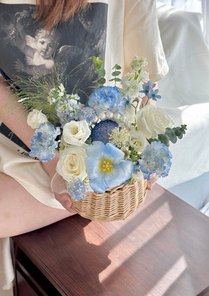Person holding a basket of blue and white flowers indoors.