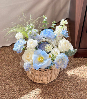 Floral arrangement in a woven basket on a carpeted floor.