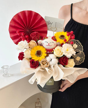 A black box adorned with flowers and a red fan, featuring a lucky cat, perfect for a grand opening celebration.