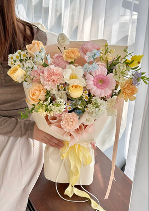 Bouquet of flowers held by a person with a white curtain background, perfect for birthdays or anniversaries.