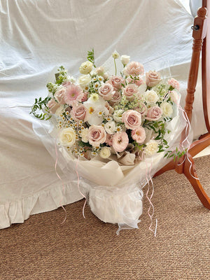 Elegant L plus size bouquet featuring quicksand roses, white gerberas, and orchids wrapped in premium white paper.