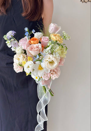 Romantic pastel wedding bouquet with roses, carnations, orange rose spray, white tulip and delicate ribbon wrap.