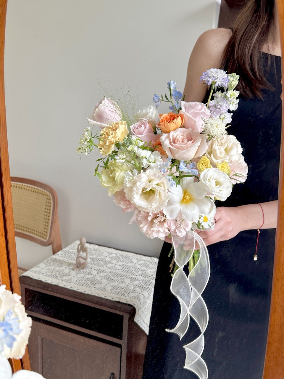 Bouquet of wedding flowers held by a person in a room with a mirror and table.