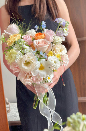 Elegant wedding bouquet with pastel roses, cream carnations, and light blue fillers tied with organza ribbon.